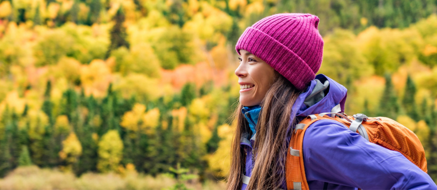 Photo of person with long dark hair and a bright pink hat smiling outdoors