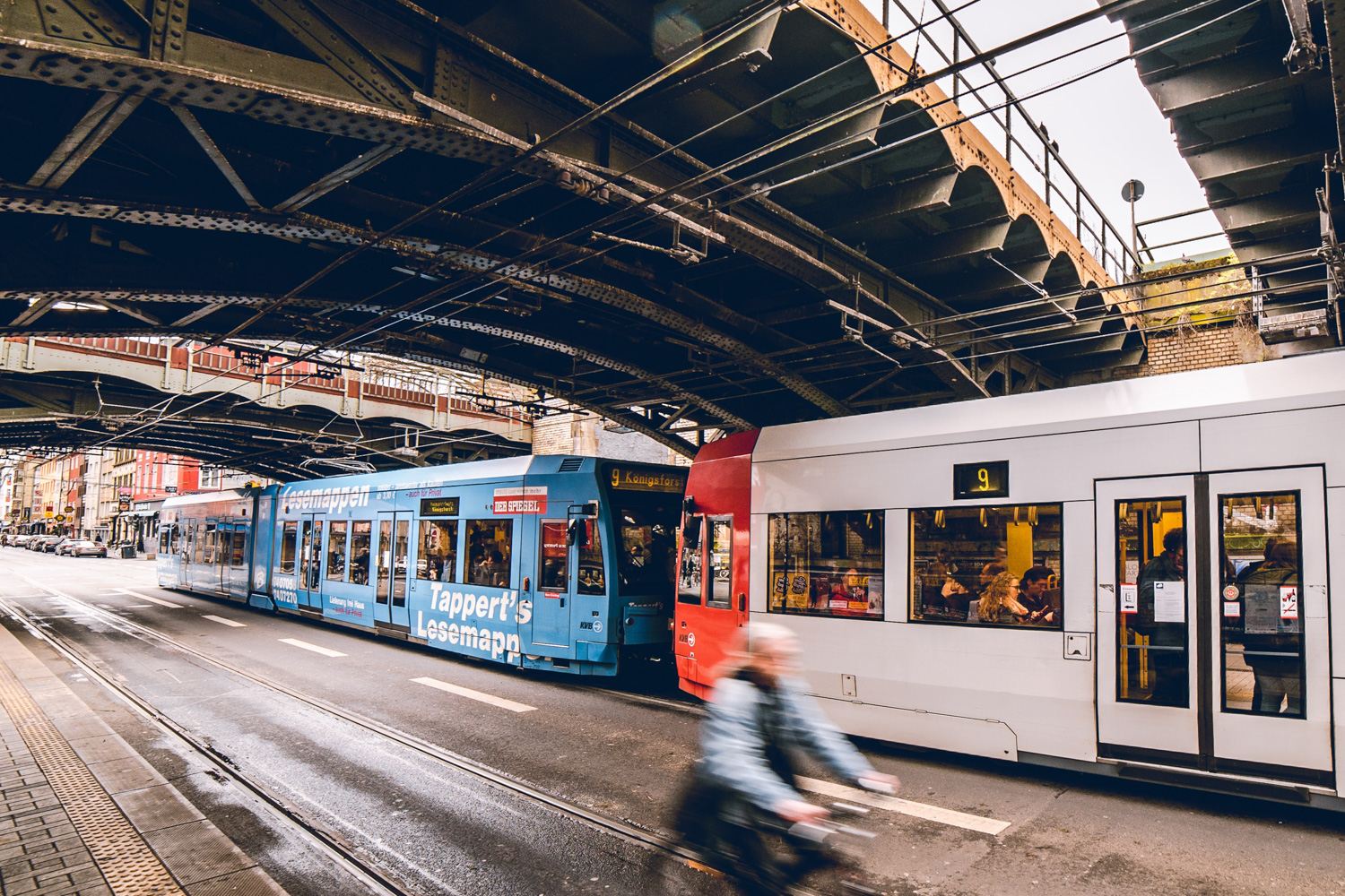 Trains, parked cars, and bicyclist in city scape. Photo Mika Baumeister via Unsplash.