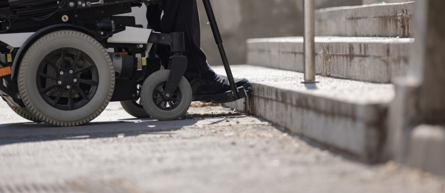 Photo of person in a powerchair looking at a set of stairs with no ramp