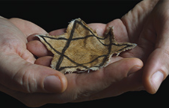 Screen capture of article photo of hands holding Star of David patch